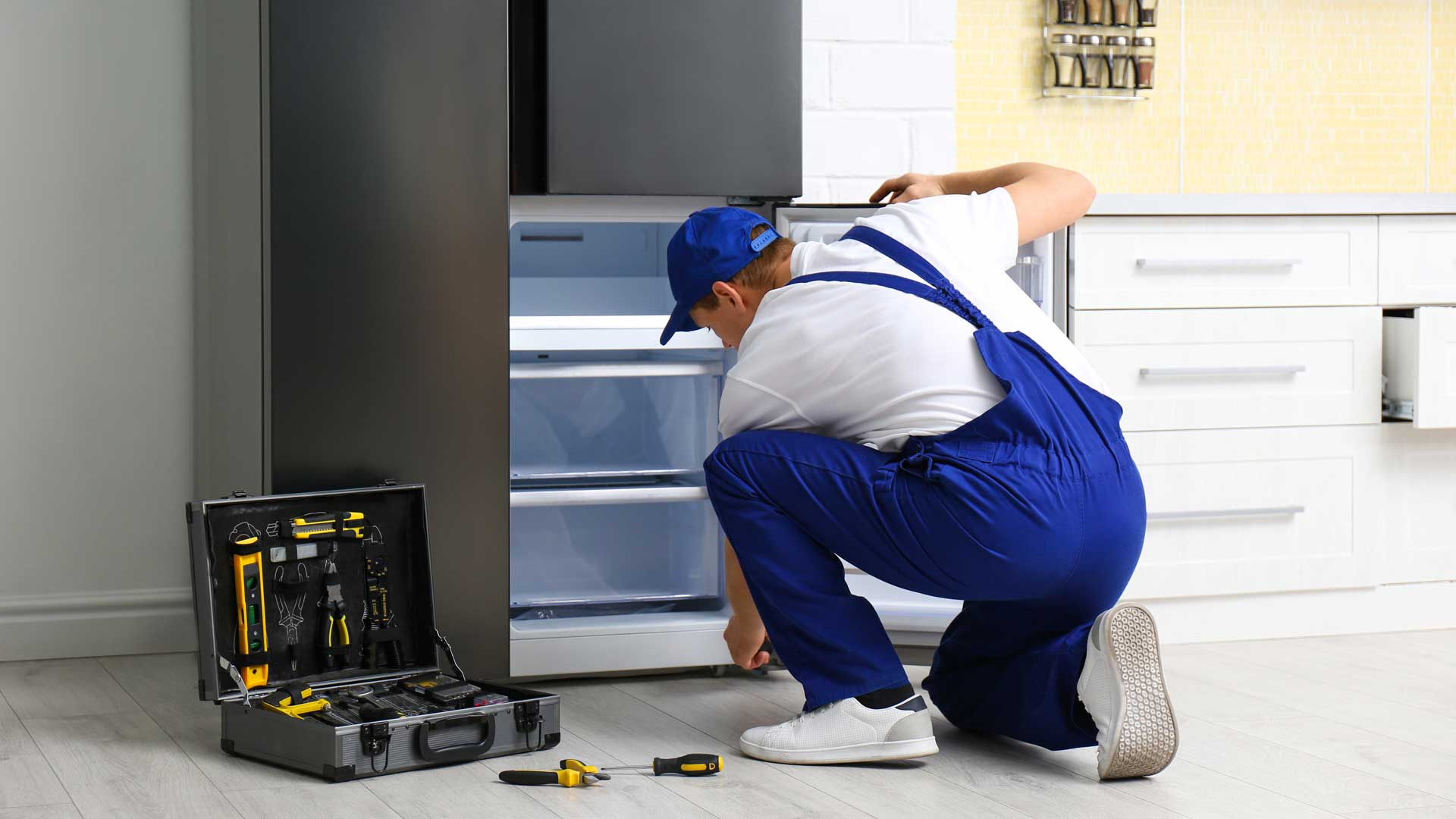Technician kneeling to repair freezer drawer on refrigerator